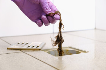 Water drain hole is clogged with hair clump. Woman hand in gloves is cleaning the bathroom sewer...