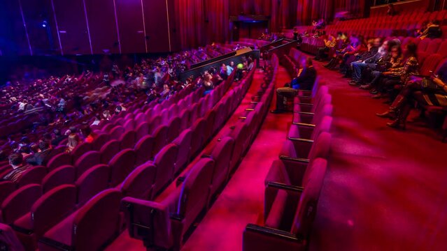 Spectators gather in the auditorium and watch the show in theatre timelapse. Large hall with red armchairs seats. Viewers filling places until turn off the light. View from right side