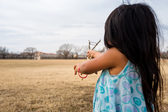 Girl in field shooting a rock from a homemade slingshot