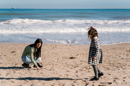 Mother drawing on sand for daughter