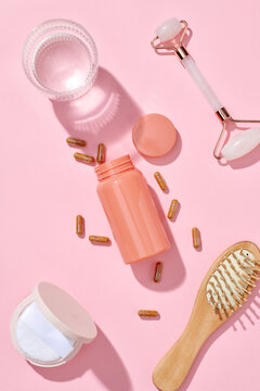 Pink quartz face roller, serum capsules on pink background.