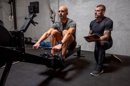 Trainer controlling sportsman on rowing machine