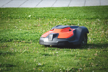 Lawn mower red robot on green cut grass on sunny day in a park