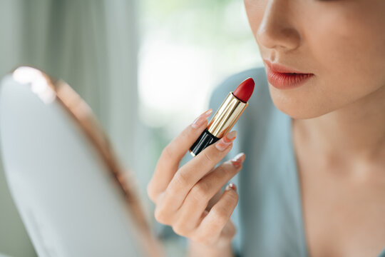 A beautiful elegant woman applying lipstick using a mirror