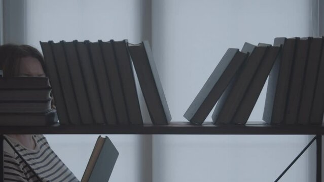 A woman in the library walks past a row of books in search of a new edition. Silhouette of a woman against the background of a bookshelf.