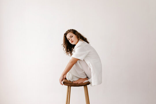 Dreamy Woman Sitting On Bar Stool Near White Wall