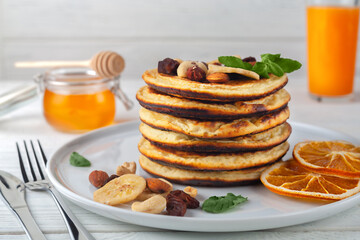Fresh, delicious pancakes with dried bananas, oranges, nuts and honey on a plate.