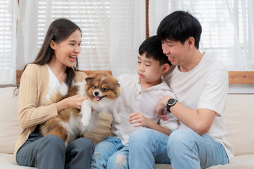 Group of Asia family sitting on the sofa in the living room at modern home with pomeranian. Boy stroking dog's back and enjoying on the weekend with father and mother. Relationship bonding concept