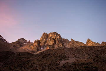 MT KENYA, KENYA. Early morning alpine glow lights up cliffs on the face of a cluster of rocky peaks in a dry environment.