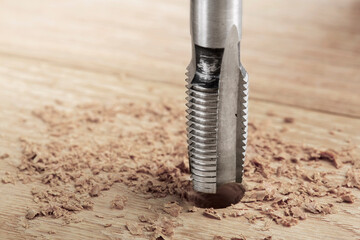 Thread tap drill cutting hole in wooden plate. Working cutter.