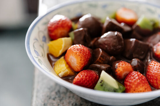 Bowl with pieces of fresh fruits and liquid chocolate in home kitchen
