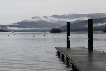 Jetty on lake Windermere with fog rolling over the mountains