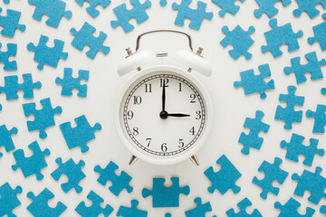 Different many blue puzzle pieces around white alarm clock on table background. Closeup. Spending time concept. Top down view.