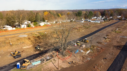 Aerial view heavy machines for foundation and earthmoving works at mobile home park construction site near row of completed manufactured trailer houses in Rochester