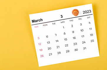 A March 2023 calendar and wooden push pin on yellow background.