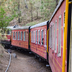 Obraz premium Toy Train moving on mountain slopes, beautiful view, one side mountain, one side valley moving on railway to the hill, among green natural forest. Toy train from Kalka to Shimla in India, Indian Train