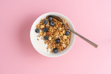 Granola with oatmeal, hazelnuts, almonds, blueberries and yogurt in white bowl on pink background. Morning healthy fast homemade breakfast concept