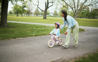 Kids, bike and a mother teaching her daughter how to cycle in a park while bonding together as a...