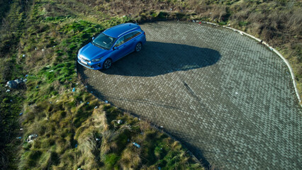 A blue car standing in a cobblestone parking place. Garbage thrown nearby. Aerial drone, top down view.
