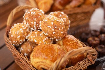 Some delicious french traditional chouquettes together with sweet pain au chocolat in a wooden basket near a few canelé dessert on a rustic table ready for breakfast in a fancy café