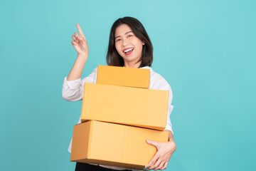Happy Asian woman holding package parcel box and pointing finger to empty copy space isolated on light green background,