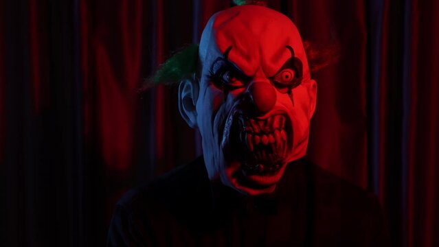 dangerous clown with horror mask in font of curtain red light 
