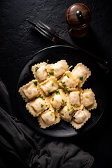 Meat dumplings - russian pelmeni, ravioli with meat in black plate on Dark grey black slate background