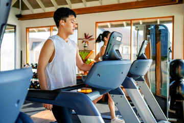Young Asian man running on treadmill in fitness