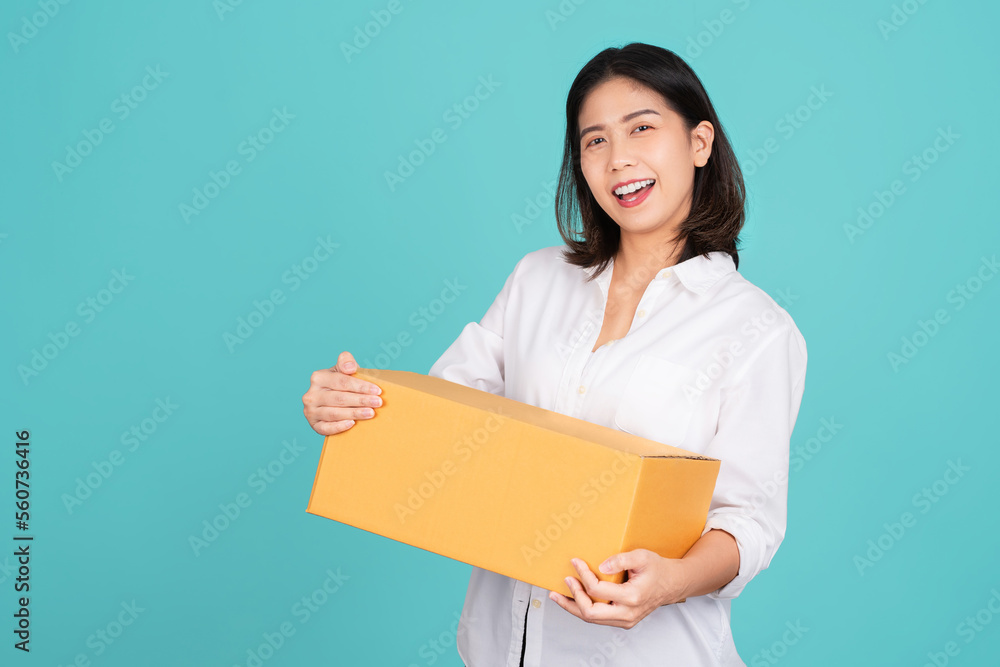 Wall mural Happy Asian woman smiling in white casual dress standing smiling and looking at camera. She is holding package parcel box isolated on light green background.