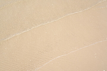 Ocean wave on tropical beach with golden sand and ripple of water splash from emerald blue-green sea water during summer vacation. 