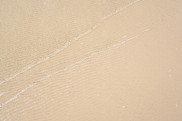 Ocean wave on tropical beach with golden sand and ripple of water splash from emerald blue-green sea water during summer vacation. 