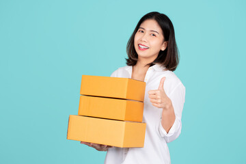 Young excited beautiful asian woman with many parcel cardboard standing on isolated light green background.