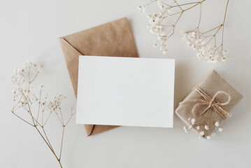 Greeting card mockup, envelope, gift box and  dried gypsophila flowers twigs on beige background...