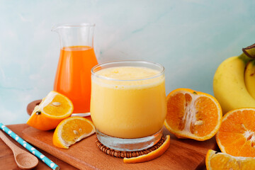 Orange fruit smoothie in a glass with fresh orange slices on wood