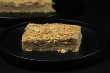Napoleon cake on a black plate on a black background. homemade baking