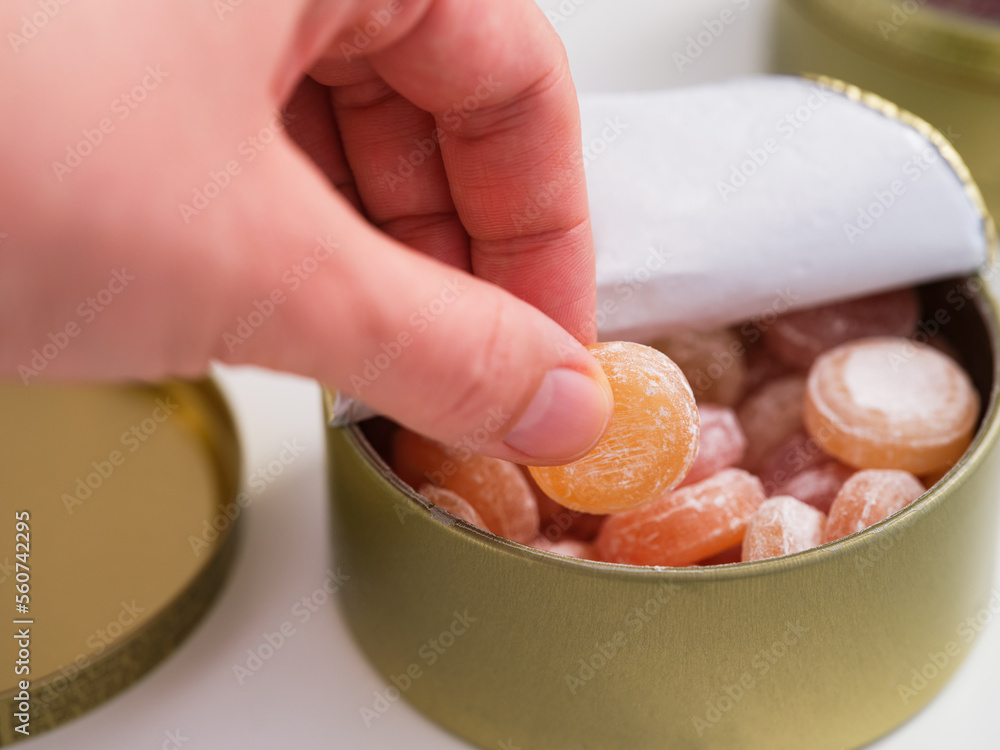 Poster Woman hand taking a candy from a tin box full of fruit drops candies