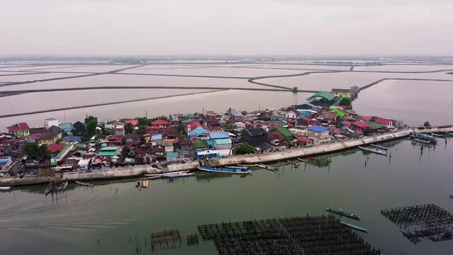 Aerial footage of fish pond in Paombong, Bulacan, Philippines. Shot on DJI Mini 2. Establishing shot showing a fishing village with houses surrounded by fishpond. Cloudy skies and vast waters.
