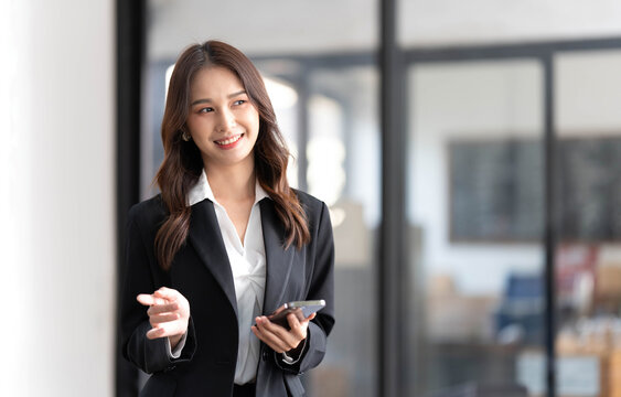 Image of a young Asian businesswoman standing using mobile phone at the office.