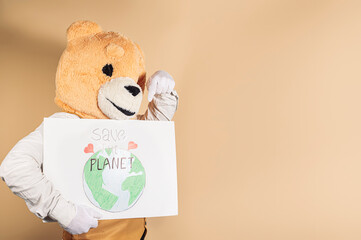 Man in a teddy bear mask on a yellow background points to a cardboard sign that reads: 'Save the...
