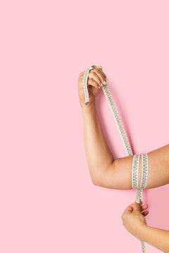 Una mujer con una cinta m&eacute;trica alrededor del brazo que tiene exceso de grasa sobre un fondo rosa pastel liso y aislado. Vista de frente y de cerca. Copy space. Formato vertical