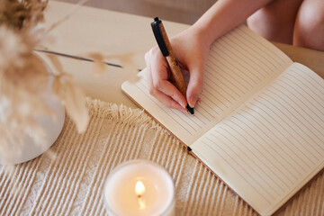 Hand, candle and woman writing in journal with top view for calm, peace mindset and relax morning routine in home. Hands, notebook and diary planning goals, idea vision or creative writer lifestyle - obrazy, fototapety, plakaty