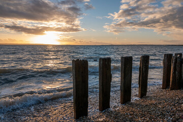 bright orange sunset over the waves and groynes in the sea on a deserted beach at Hill Head Hampshire England