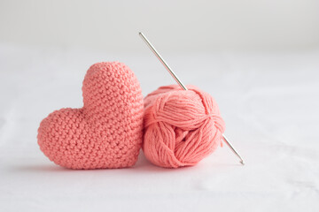 Crocheted amigurumi pastel pink heart with crochet hook and skein of yarn on a white background. Valentine's day banner with copy space, gift with love symbol, handcraft for health concept