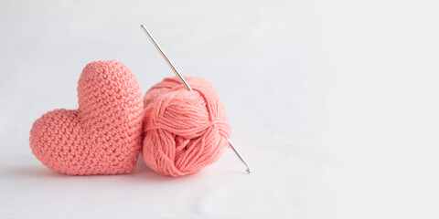 Crocheted amigurumi pastel pink heart with crochet hook and skein of yarn on a white background....