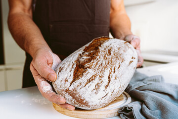 Rye craft homemade bread in muscular textured hands of male baker