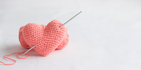 Crocheted amigurumi pink heart with crochet hook and skein of yarn on a white background....