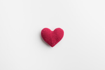 Crocheted amigurumi pink red heart on a white natural solid background, top view with empty space....