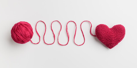Crocheted amigurumi pink heart with a ball of yarn on a pastel pink background. Valentine's day...