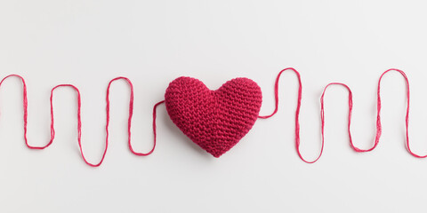 Crocheted amigurumi pink red heart with a cotton waved thread on a white background. Valentine's...