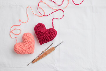 Two crocheted amigurumi pink hearts with a crochet hooks on a white background. Valentine's banner top view - obrazy, fototapety, plakaty